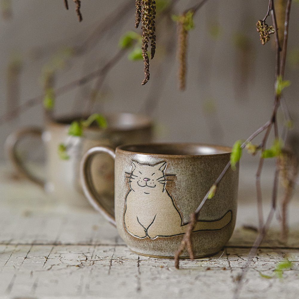 Handmade green ceramic mug with a matt glaze, featuring an unglazed cat design on the side.