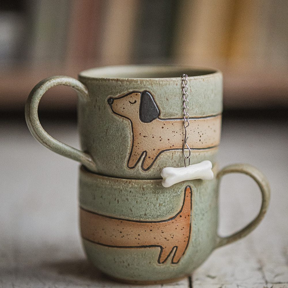 Tea infuser in the cup with white ceramic bone hanging from the chain