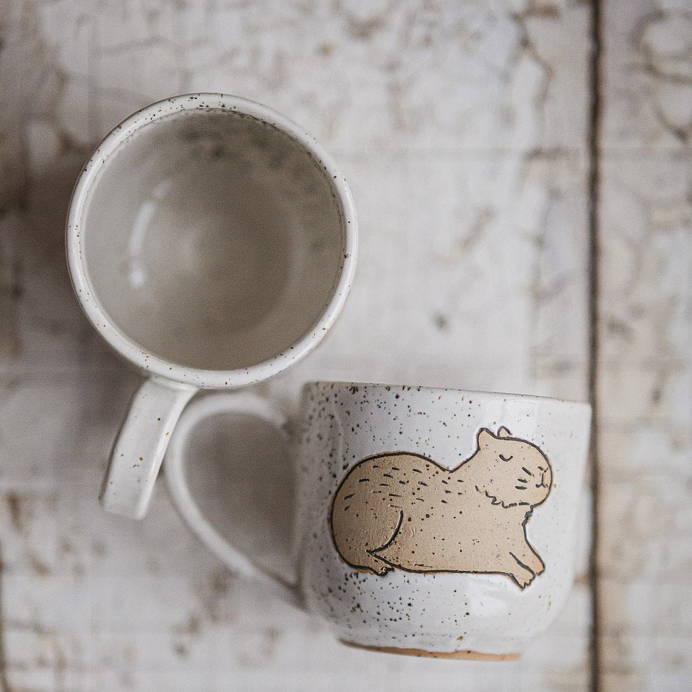 Handmade white ceramic mug with a matte glaze, featuring an unglazed lying capybara design on the side.