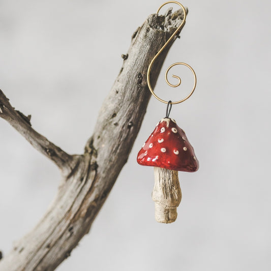 Red amanita ceramic mushroom ornament hanging on a branch of Christmas tree.