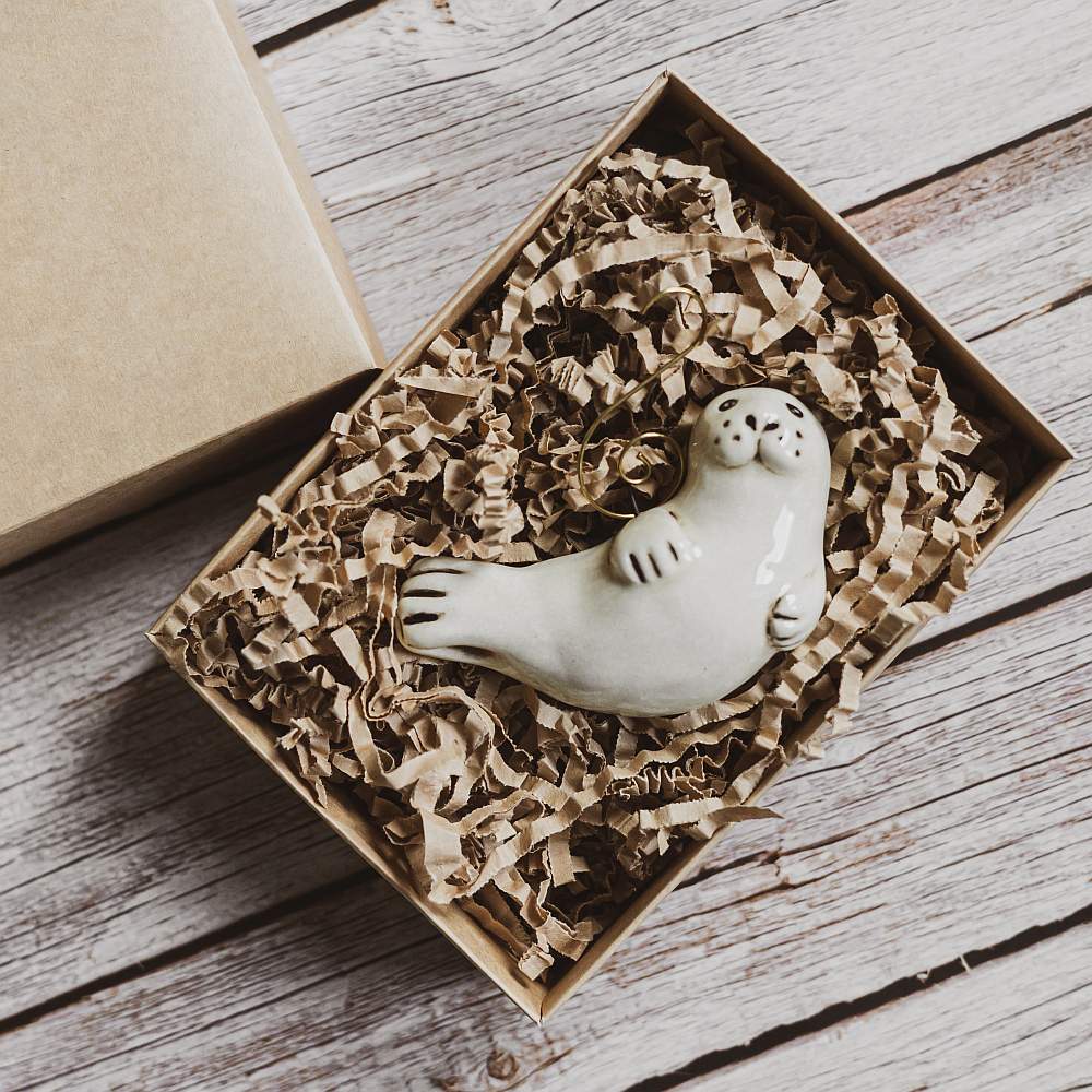 A ceramic seal ornament with black painted eyes, nose and tail. The decoration is handmade and comes with yellow hook.