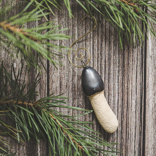 Ceramic stinkhorn mushroom with mat black cap and cream-colored stem. Handmade Christmas tree ornament with hook.