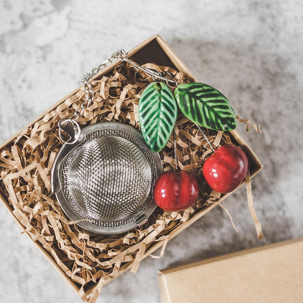 Tea infuser with ceramic cherries with leaves hanging from the chain. Packed in a paper gift box.