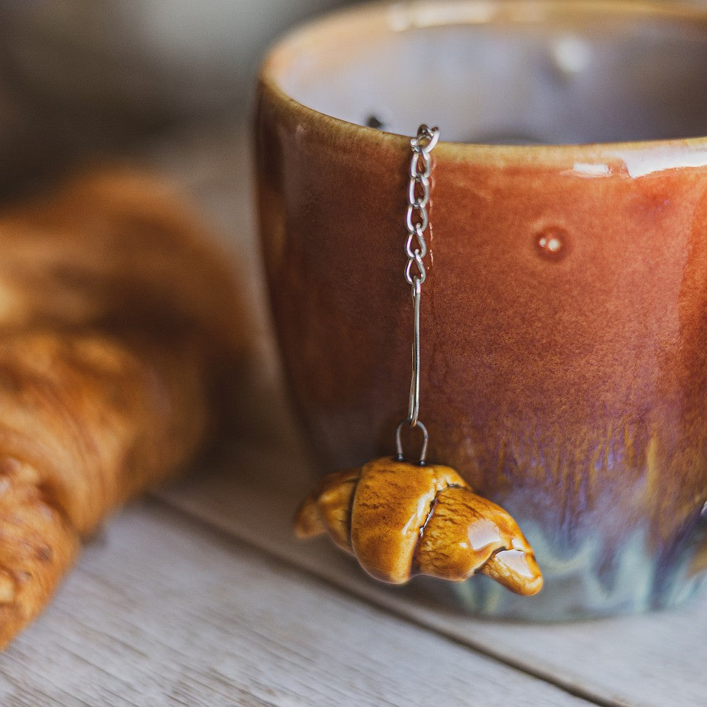 Tea infuser in the cup with ceramic croissant hanging from the chain