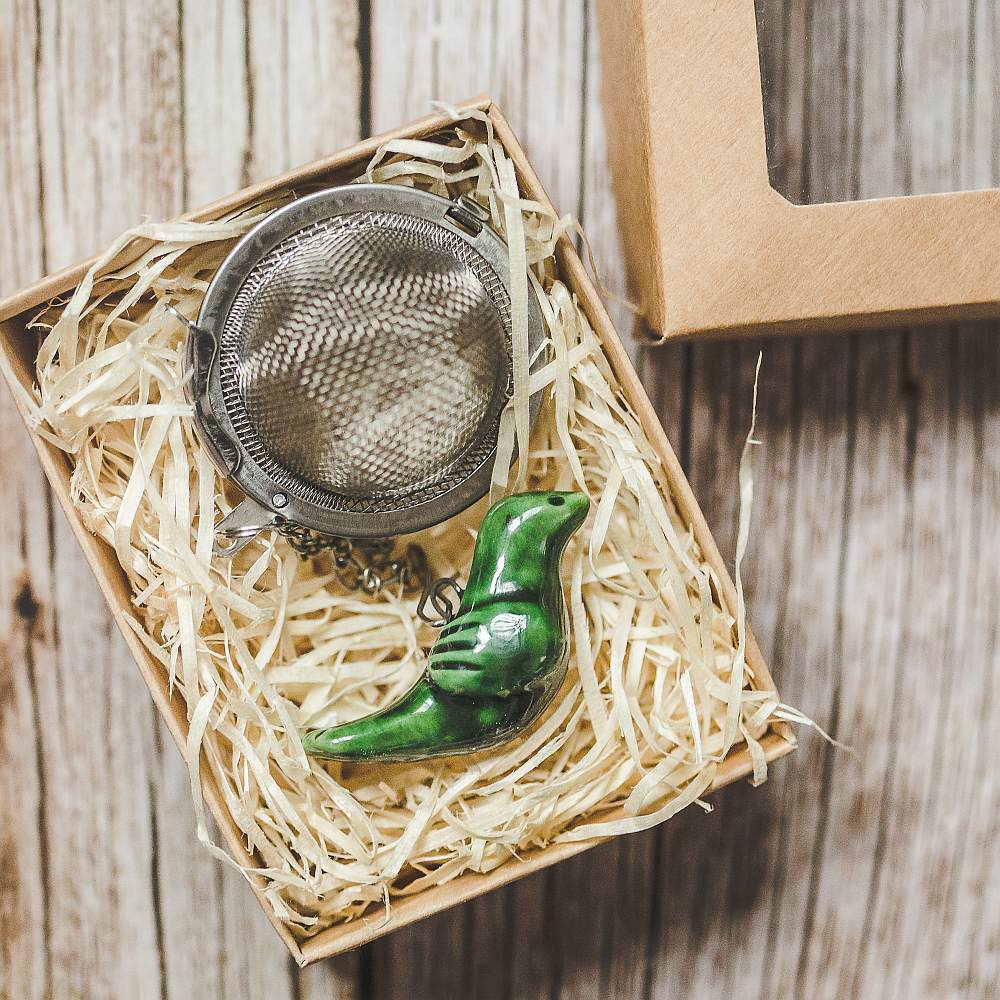 Tea infuser with ceramic green bird hanging from the chain. Packed in a paper gift box.