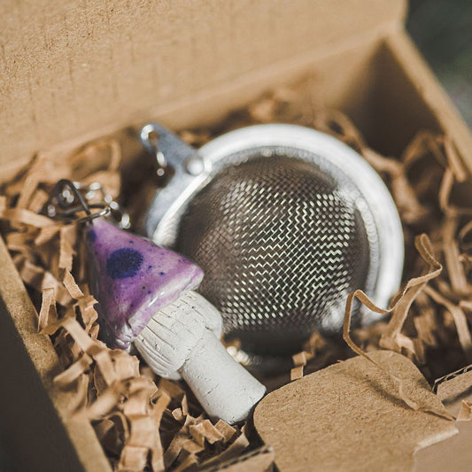 Tea infuser with ceramic purple mushroom hanging from the chain. Packed in a paper gift box.