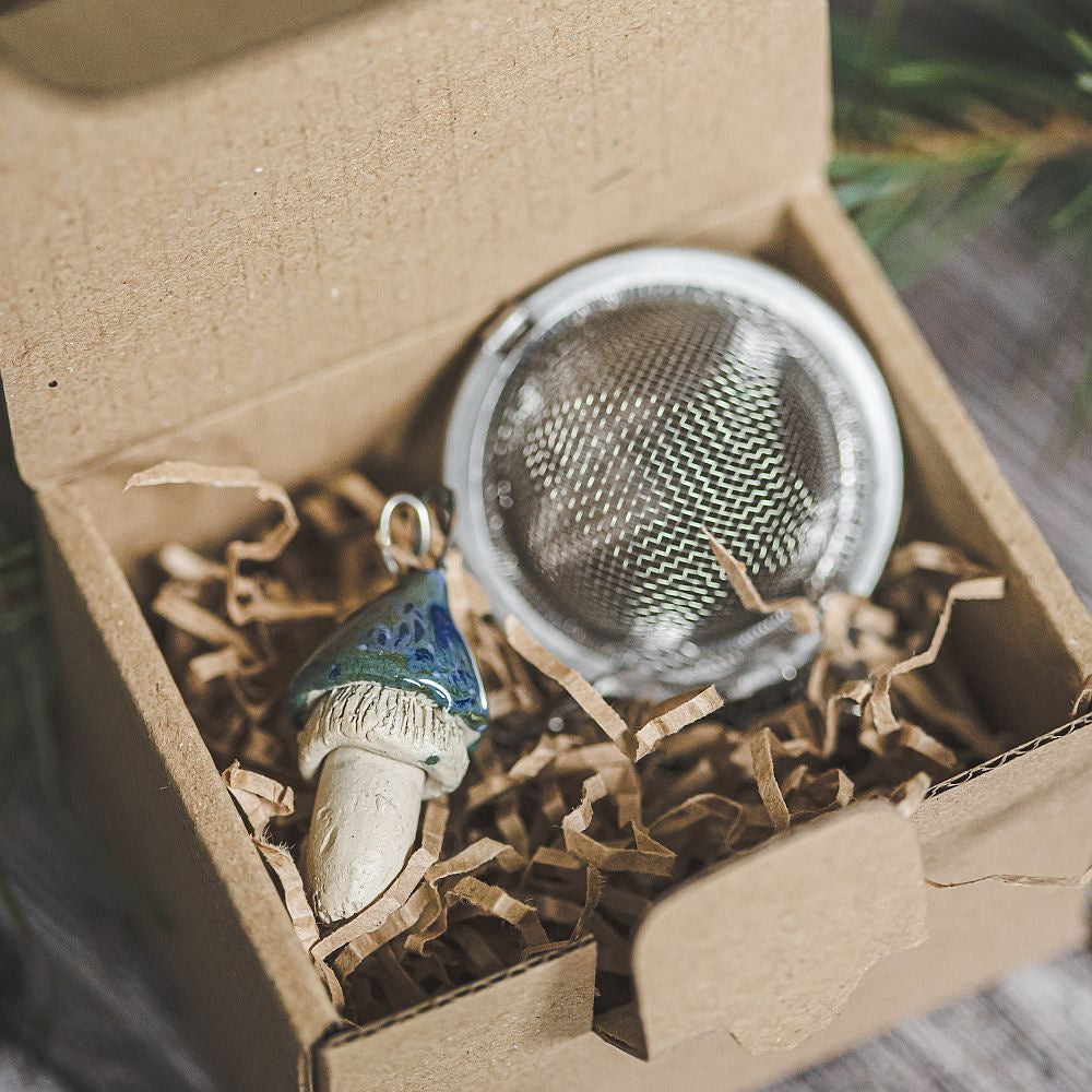 Tea infuser with ceramic swamp blue mushroom hanging from the chain. Packed in a paper gift box.