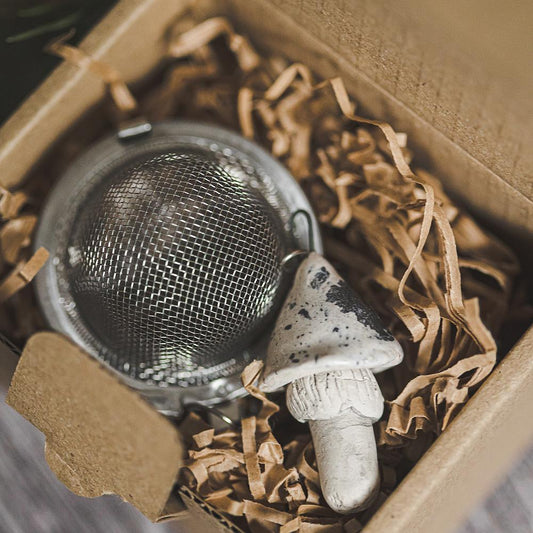 Tea infuser with ceramic white dotted mushroom hanging from the chain. Packed in a paper gift box.