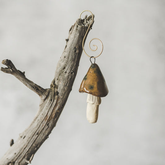 Ceramic brown swamp mushroom ornament hanging on a branch of Christmas tree.
