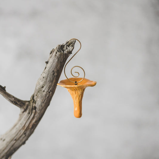 Chanterelle ceramic mushroom ornament hanging on a branch of Christmas tree.