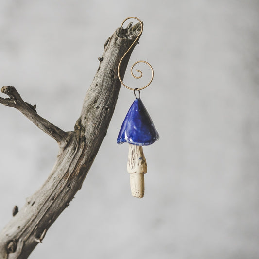 Ceramic dark blue mushroom ornament hanging on a branch of Christmas tree.