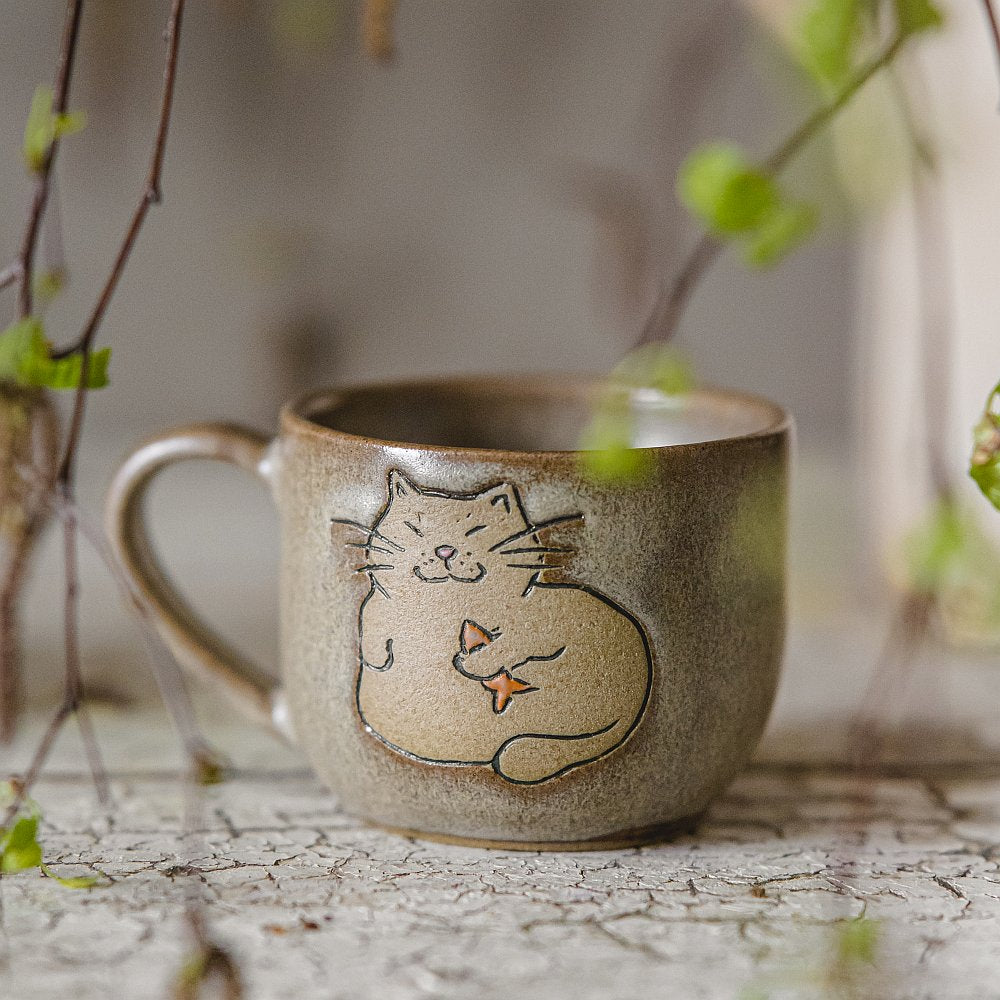 Handmade green ceramic mug with a matt glaze, featuring an unglazed cat design on the side.