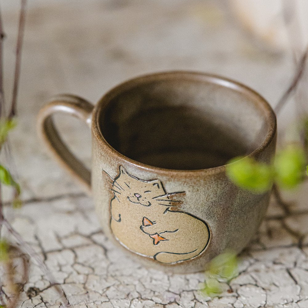 Handmade green ceramic mug with a matt glaze, featuring an unglazed cat design on the side.