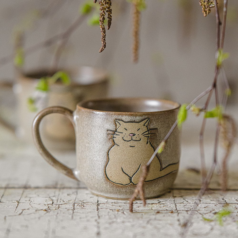 Handmade green ceramic mug with a matt glaze, featuring an unglazed cat design on the side.