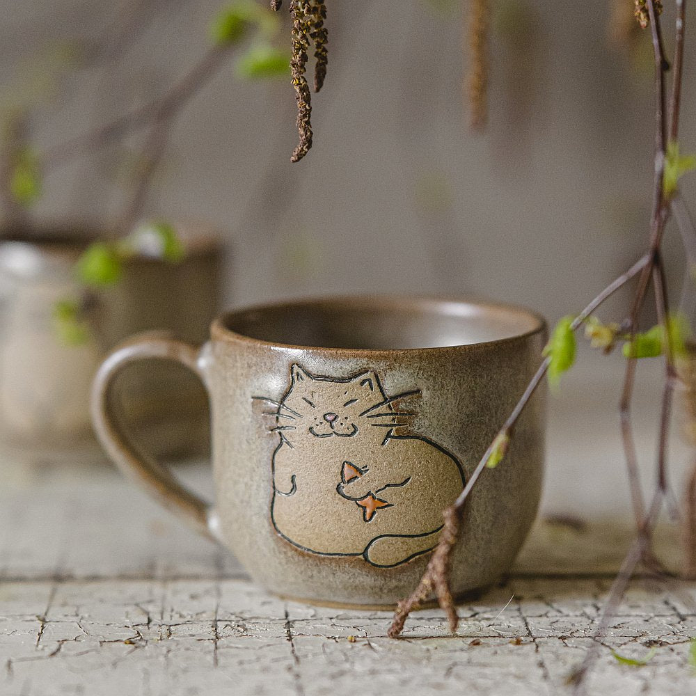 Handmade green ceramic mug with a matt glaze, featuring an unglazed cat design on the side.
