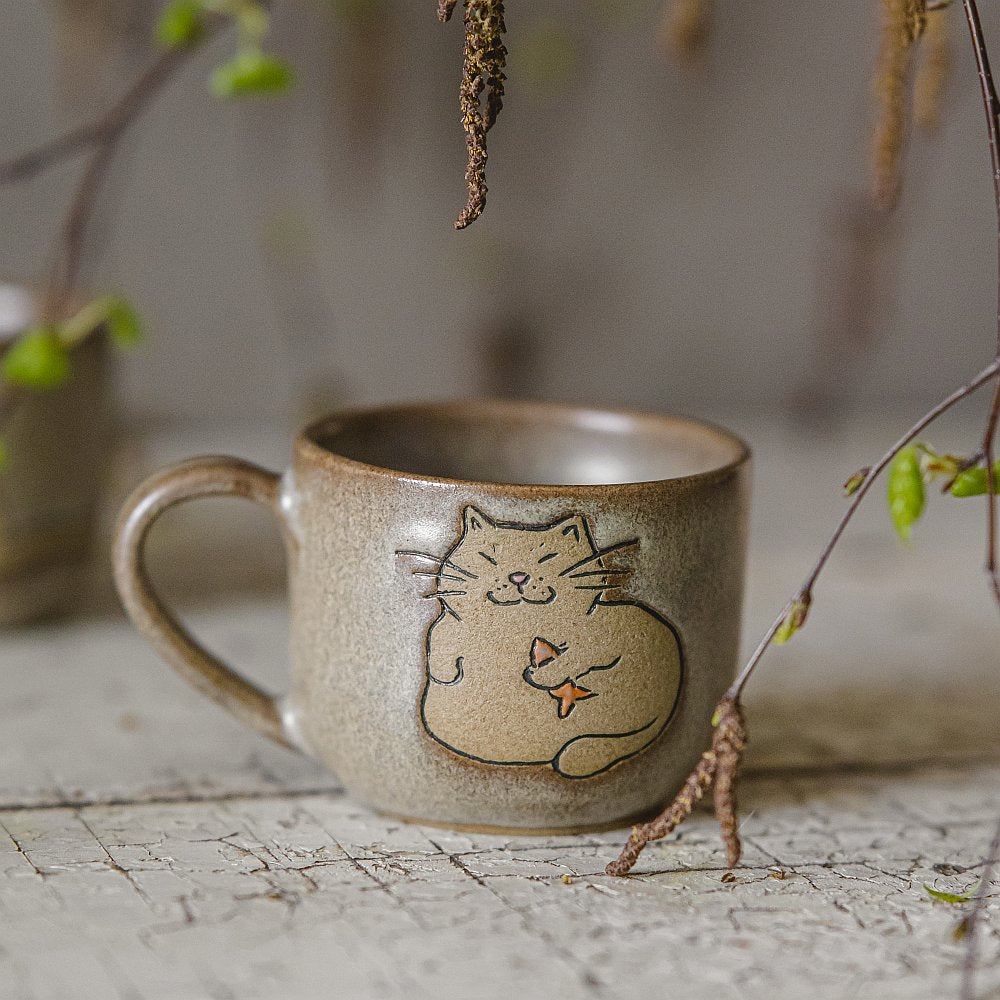 Handmade green ceramic mug with a matt glaze, featuring an unglazed cat design on the side.