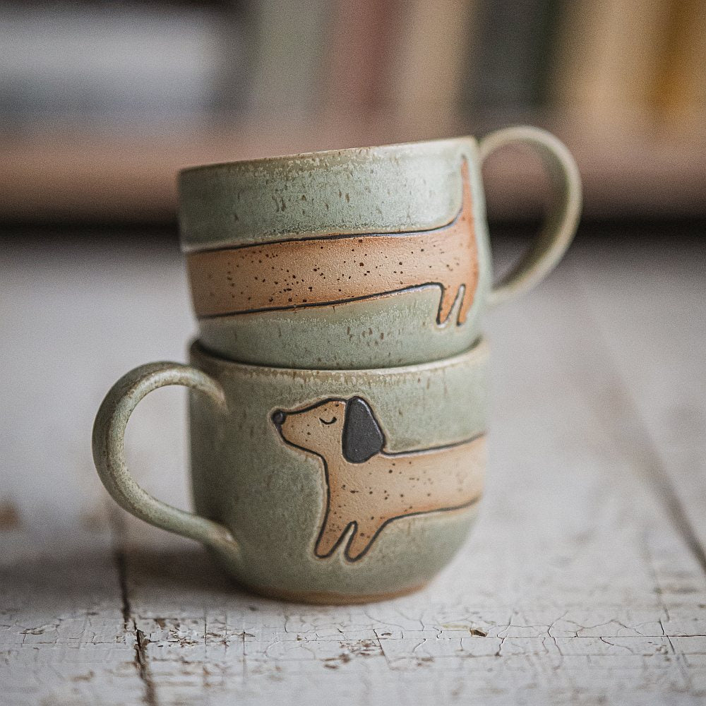 Handmade green ceramic mug with a matte glaze, featuring an unglazed dog design on the side.