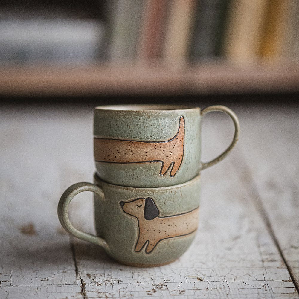 Handmade green ceramic mug with a matte glaze, featuring an unglazed dog design on the side.