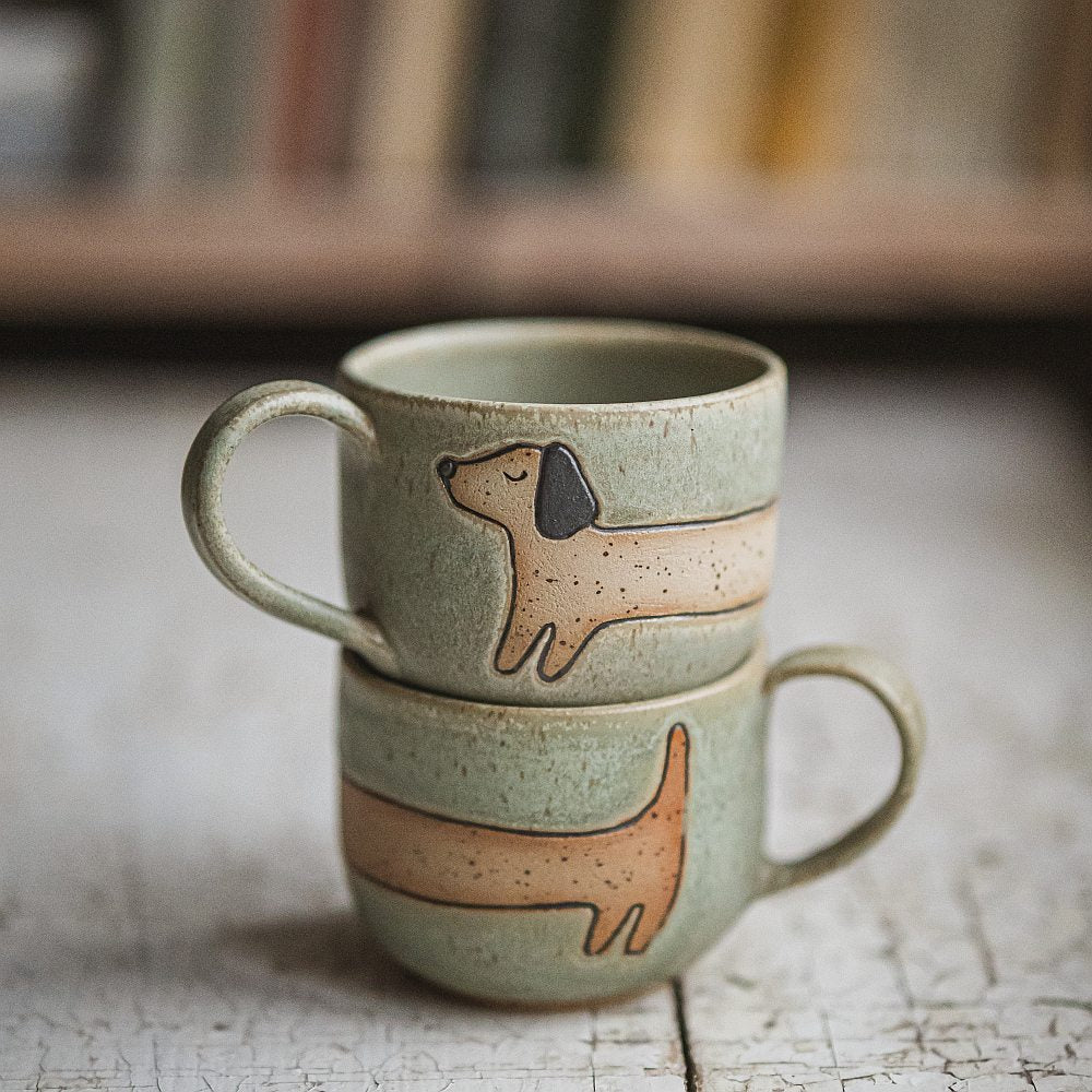 Handmade green ceramic mug with a matte glaze, featuring an unglazed dog design on the side.