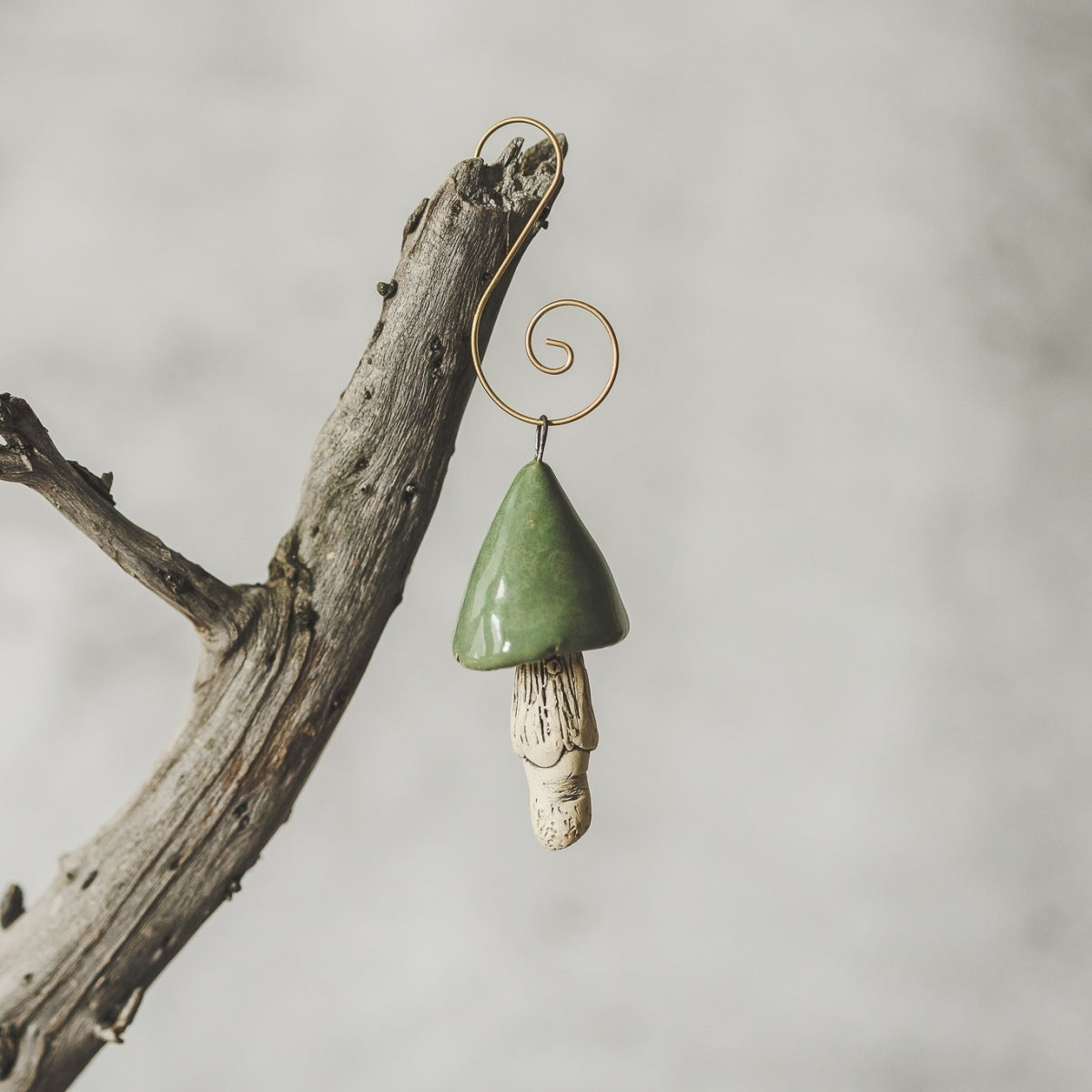 Ceramic green swamp mushroom ornament hanging on a branch of Christmas tree.