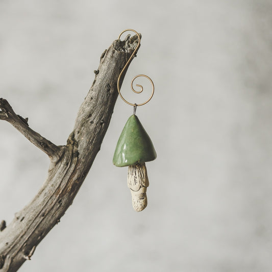 Ceramic green swamp mushroom ornament hanging on a branch of Christmas tree.