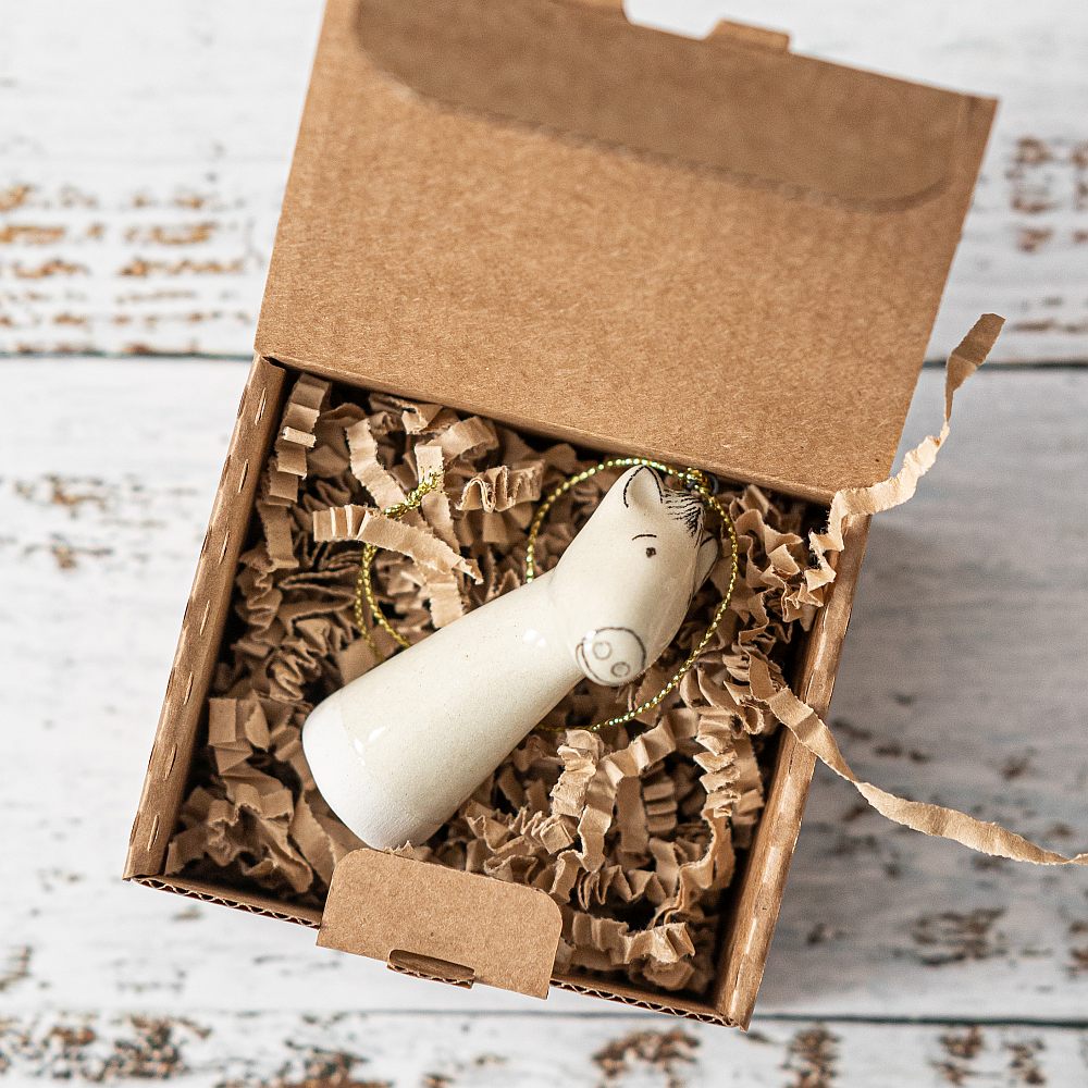 A white ceramic horse ornament with black painted eyes and a small mouth. The decoration is white with black markings and is hanging from a gold string.