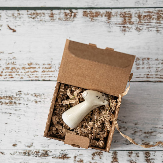 A white ceramic horse ornament with black painted eyes and a small mouth. The decoration is white with black markings and is hanging from a gold string.
