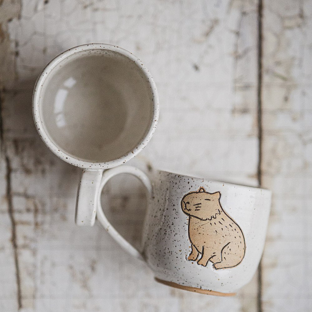Handmade white ceramic mug with a matte glaze, featuring an unglazed sitting capybara design on the side.