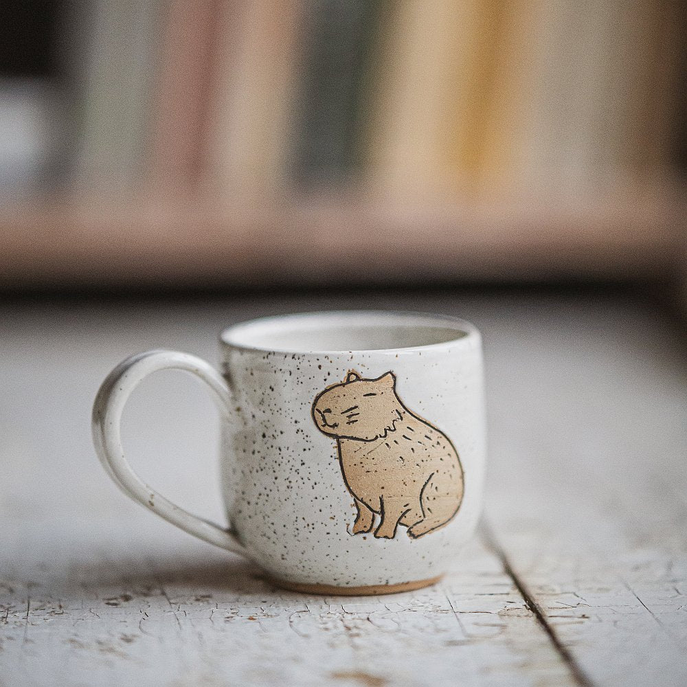 Handmade white ceramic mug with a matte glaze, featuring an unglazed sitting capybara design on the side.