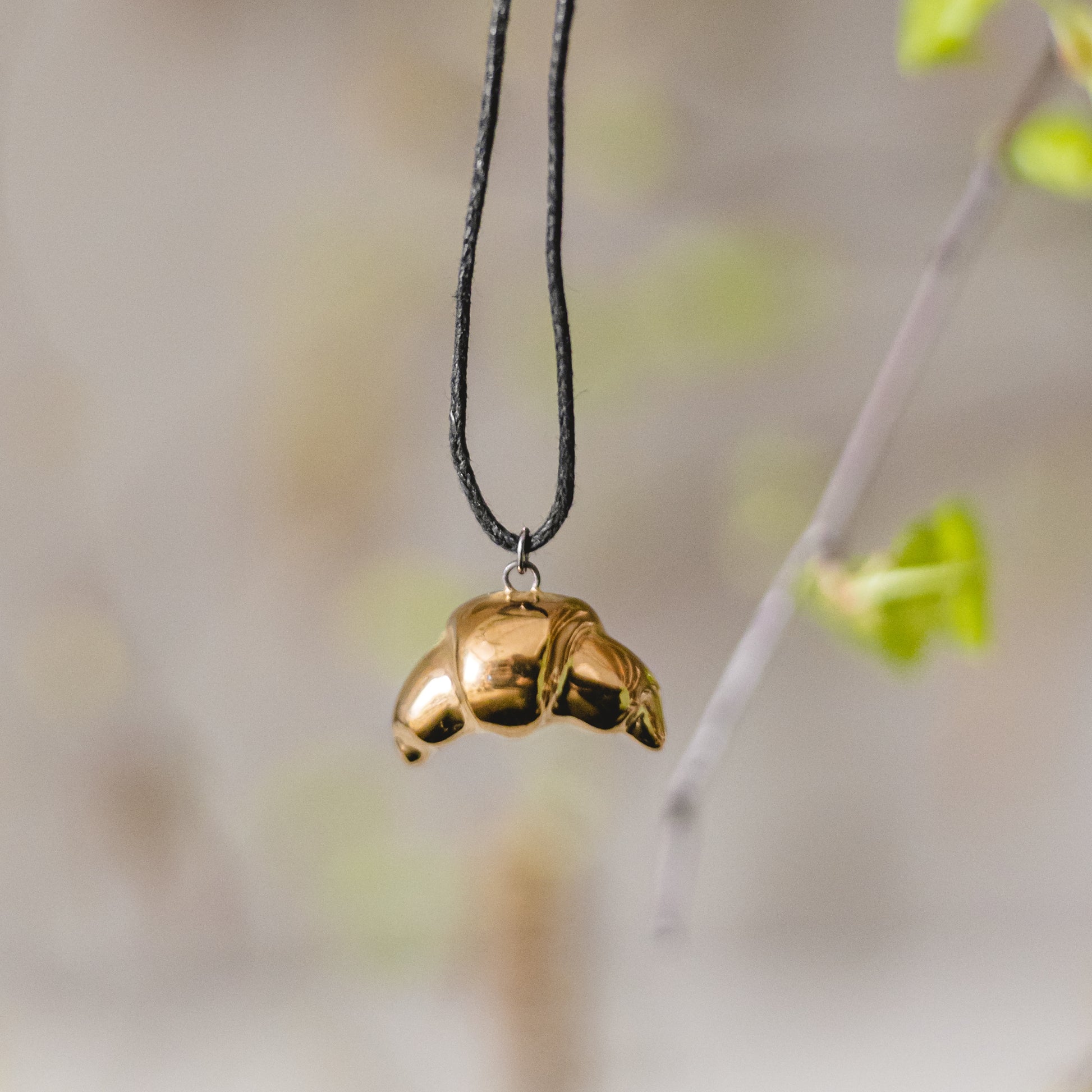 Handmade ceramic croissant pendant necklace with gold plated finish on black cord