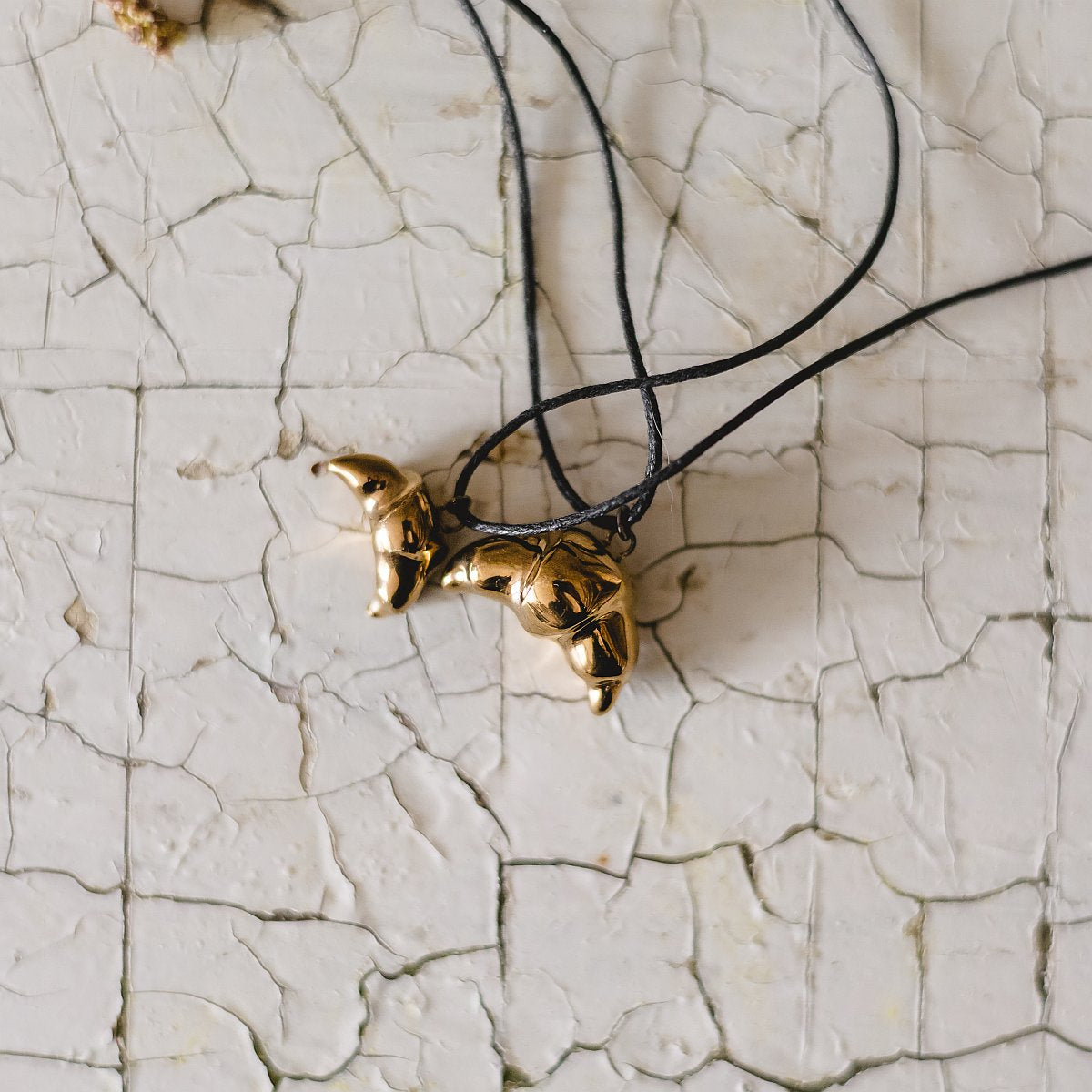 Handmade ceramic croissant pendant necklace with gold plated finish on black cord