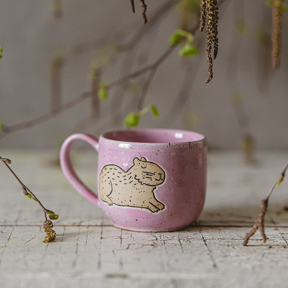 Handmade pink ceramic mug with a glossy glaze, featuring an unglazed capybara design on the side.