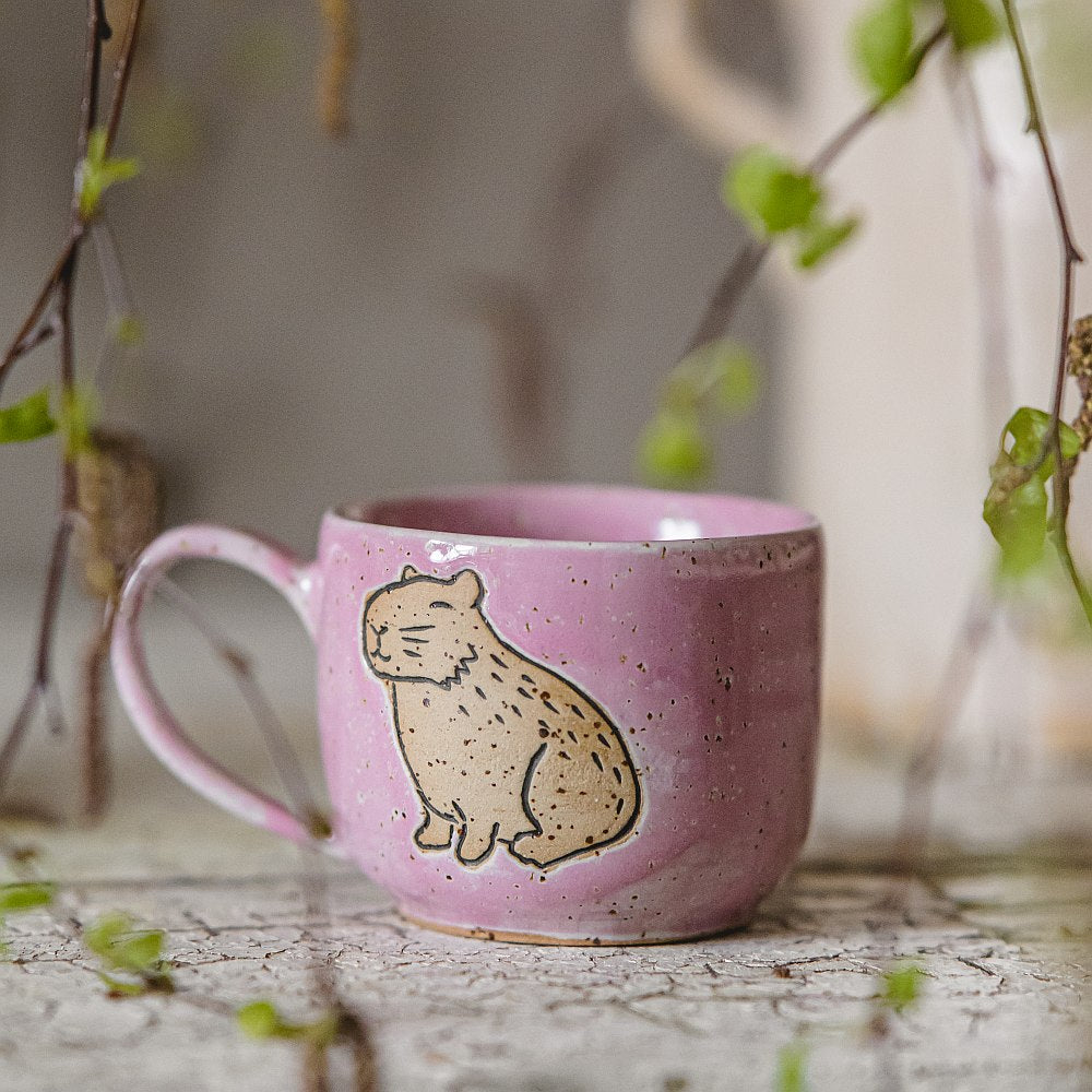 Handmade pink ceramic mug with a glossy glaze, featuring an unglazed capybara design on the side.