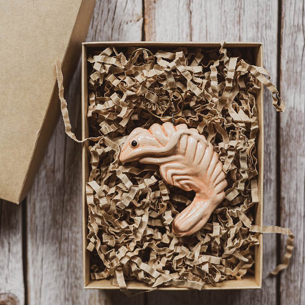 A ceramic pink shrimp ornament with black eyes. The decoration is handmade and comes with yellow hook.