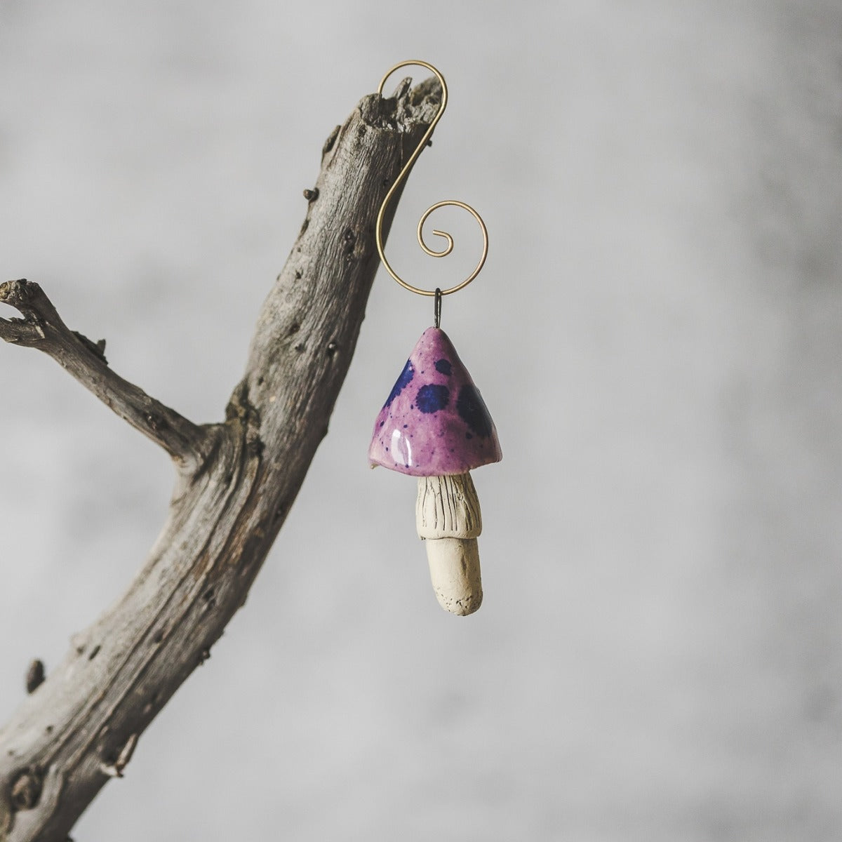 Ceramic purple magic mushroom ornament hanging on a branch of Christmas tree.