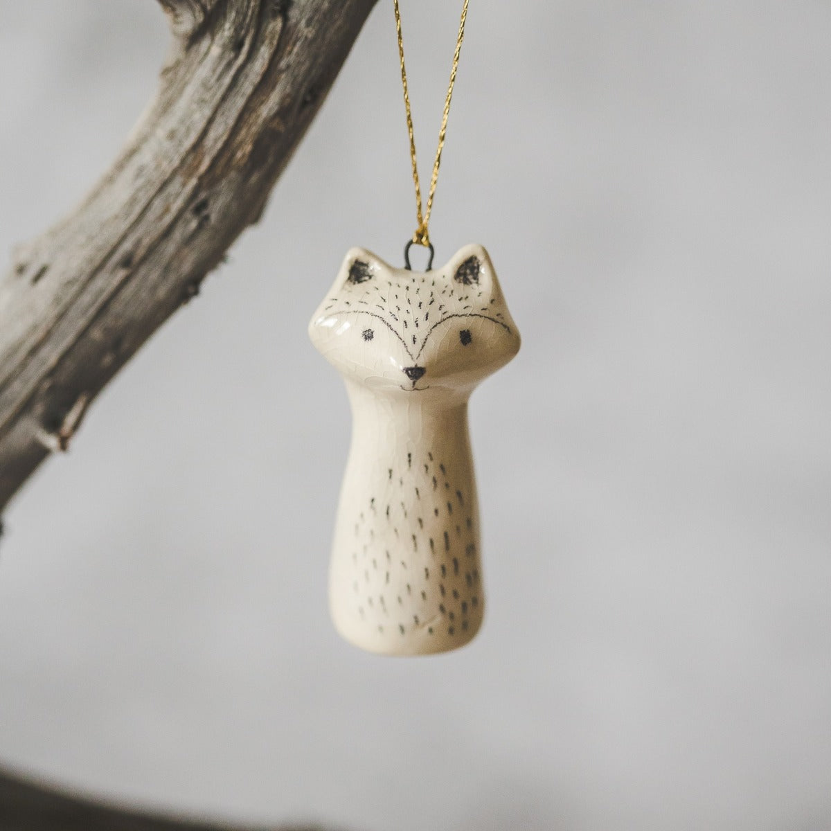 A ceramic wild raccoon ornament with hand-drawn black eyes and a black nose. The decoration is white with black markings and is hanging from a gold string.