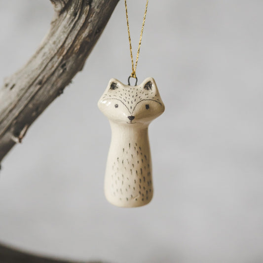 A ceramic wild raccoon ornament with hand-drawn black eyes and a black nose. The decoration is white with black markings and is hanging from a gold string.