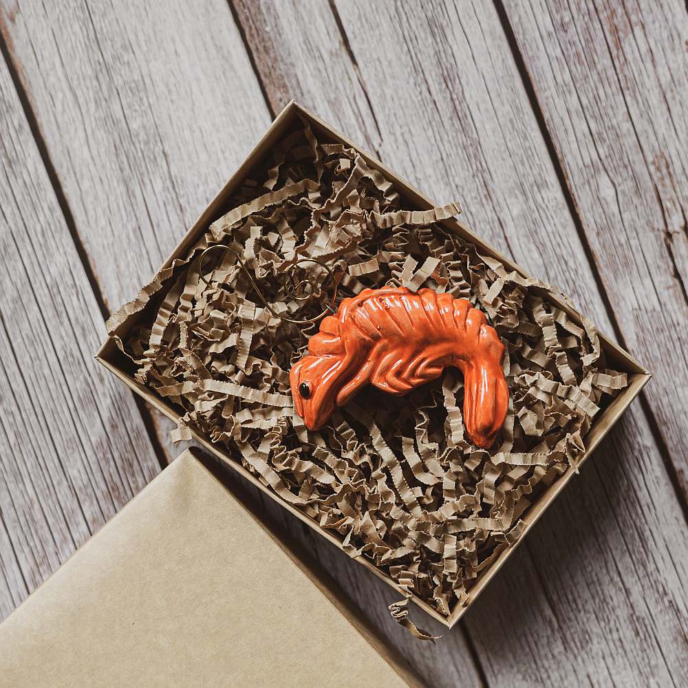 A ceramic red shrimp ornament with black eyes. The decoration is handmade and comes with yellow hook.