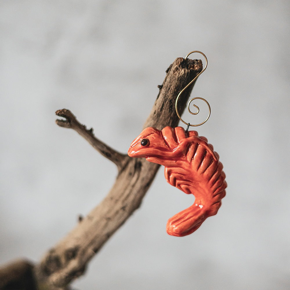 A ceramic red shrimp ornament with black eyes. The decoration is handmade and comes with yellow hook.