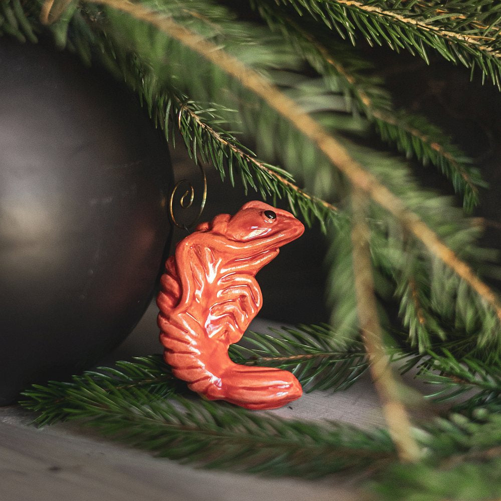 A ceramic red shrimp ornament with black eyes. The decoration is handmade and comes with yellow hook.