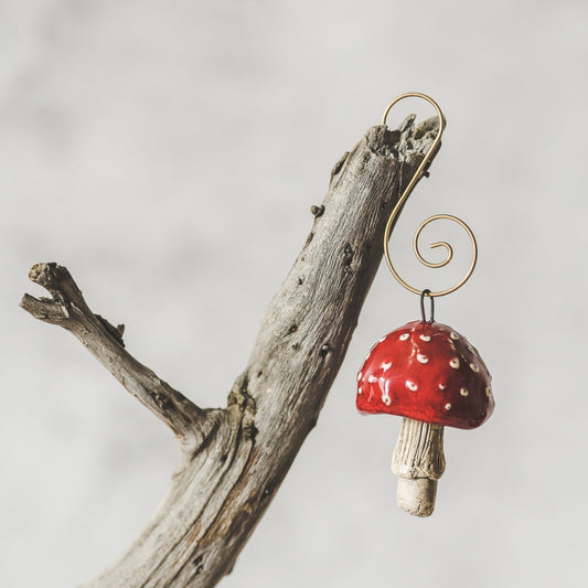 Red amanita ceramic mushroom ornament hanging on a branch of Christmas tree.