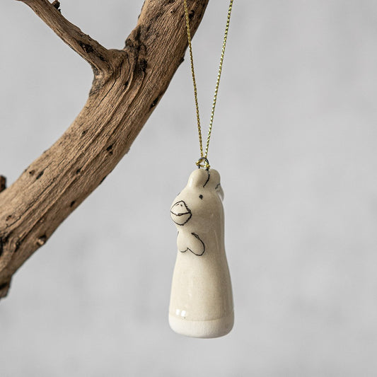 A white ceramic bunny ornament with black painted eyes and a small beak. The decoration is white with black markings and is hanging from a gold string.