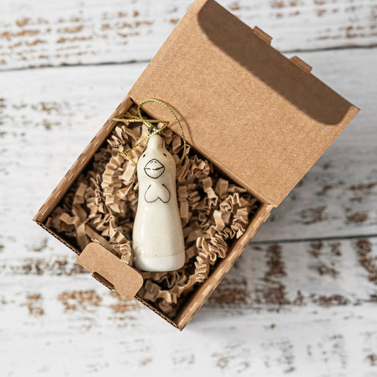 A white ceramic bunny ornament with black painted eyes and a small beak. The decoration is white with black markings and is hanging from a gold string.