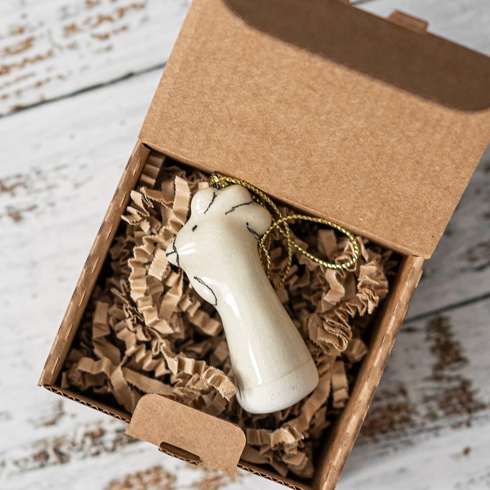 A white ceramic bunny ornament with black painted eyes and a small beak. The decoration is white with black markings and is hanging from a gold string.