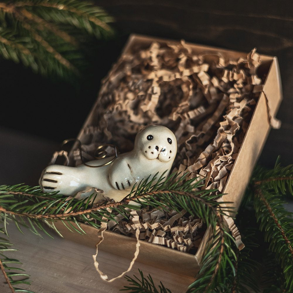 A ceramic seal ornament with black painted eyes, nose and tail. The decoration is handmade and comes with yellow hook.
