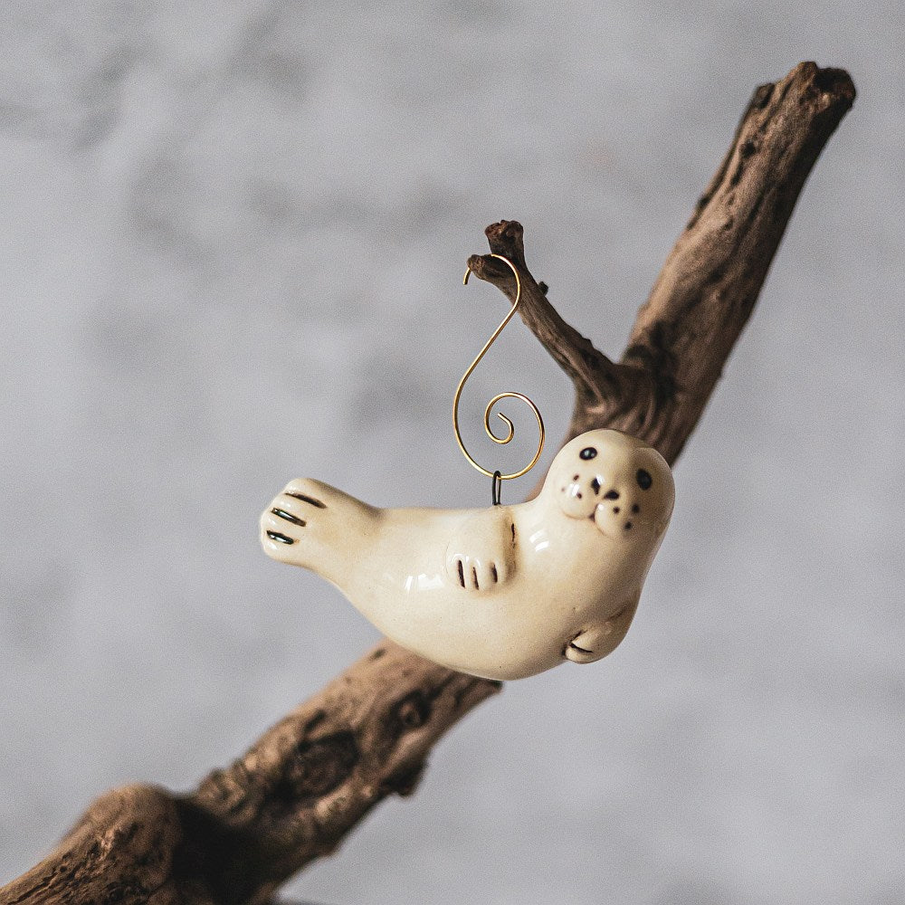 A ceramic seal ornament with black painted eyes, nose and tail. The decoration is handmade and comes with yellow hook.