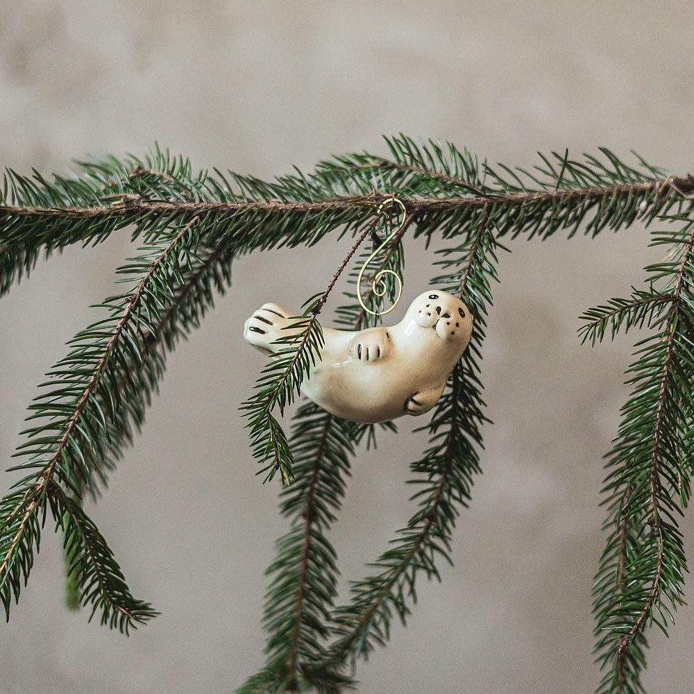 A ceramic seal ornament with black painted eyes, nose and tail. The decoration is handmade and comes with yellow hook.