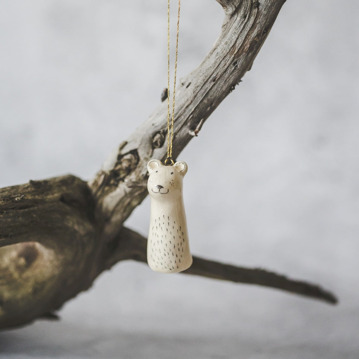 A smiling ceramic polar bear ornament with hand-drawn black eyes and a black nose. The decoration is white with black markings and is hanging from a gold string.