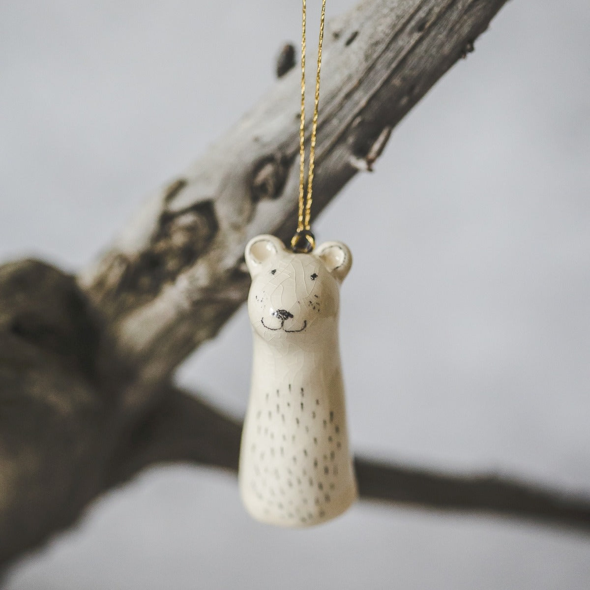 A smiling ceramic polar bear ornament with hand-drawn black eyes and a black nose. The decoration is white with black markings and is hanging from a gold string.