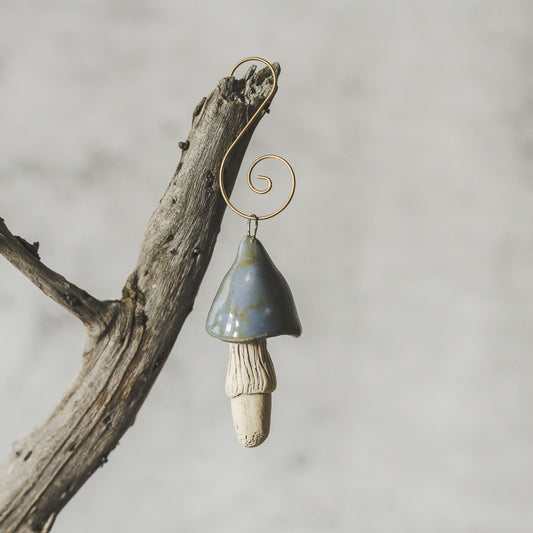 Ceramic swamp blue mushroom ornament hanging on a branch of Christmas tree.
